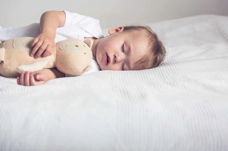 Sleeping baby in his crib, holding a teddy bear.